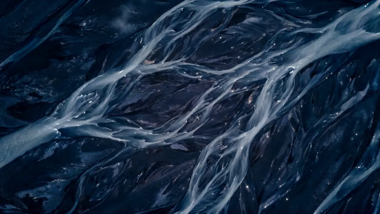 Aerial view of a braided river delta at night, pale channels splitting and rejoining across dark ground.